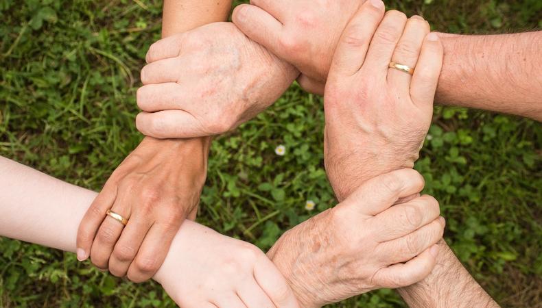 A variety of ages of hands hold each other at the wrist forming a circle.